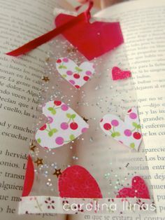 an open book with paper hearts on it and a red ribbon hanging from the top