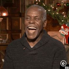 an older man laughing in front of a christmas tree