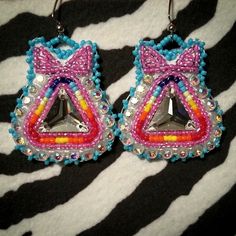 two pairs of earrings with colorful beads and bows on zebra print fabric, hanging from metal hooks