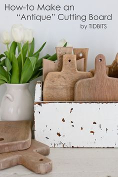 some wooden cutting boards and flowers in a white vase on a table next to other wood utensils