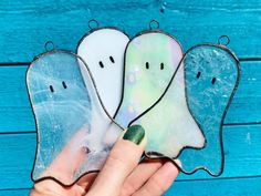 a hand holding three stained glass ghostes with their faces painted green, white and blue