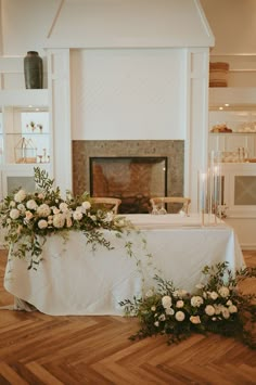 a table with flowers and greenery on it in front of a fireplace at a wedding