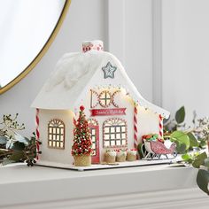 a christmas house with lights and decorations on top of a mantle next to a mirror