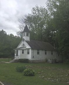 an old white church with a steeple in the middle of it's yard