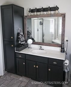 a bathroom with black cabinets and white counter tops, along with a large mirror over the sink