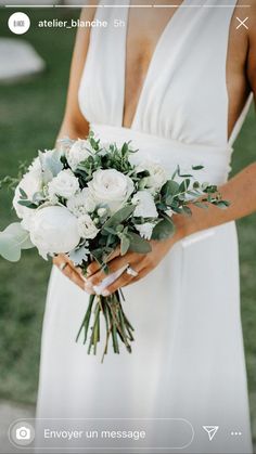 a woman in a white dress holding a bouquet of flowers and greenery on her wedding day