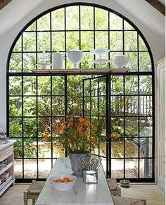 an arched window in a kitchen with white counter tops and orange flowers on the table