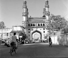 black and white photograph of two people riding bikes in front of a large building with towers