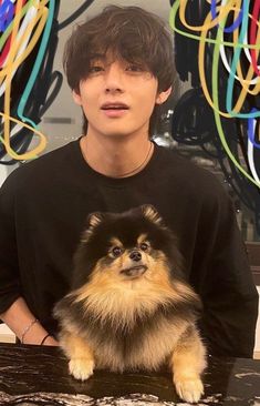 a young man sitting at a table with a dog in front of him and colorful streamers behind him