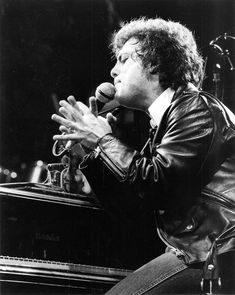 a man sitting in front of a microphone on top of a piano and holding his hands out