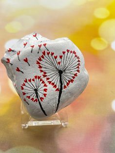 a heart shaped rock with dandelions painted on it sitting on a glass stand