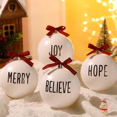 three white ornaments with red bows on them sitting on a table next to a christmas tree