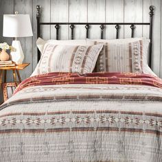 a bed with pillows and blankets on top of it next to a night stand in front of a wooden wall