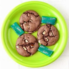 three chocolate cookies are on a green plate with mints and candy bar wrappers