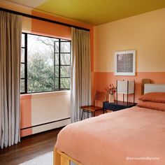 a bedroom with an orange and pink color scheme on the walls, wood flooring and large windows