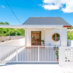 a small white house with a big front door and fenced in area next to it