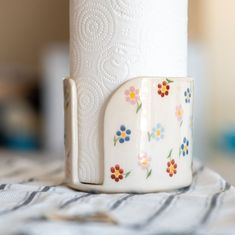 a white toilet paper holder sitting on top of a striped tablecloth with flowers painted on it