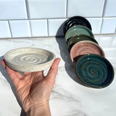 a hand is holding a small bowl in front of several bowls on a counter top