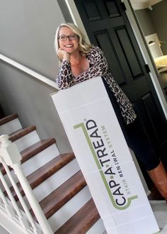 a woman standing on the stairs holding a sign that reads capital real estate, and smiling at the camera