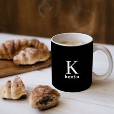 a cup of coffee next to some croissants on a cutting board with steam rising from them