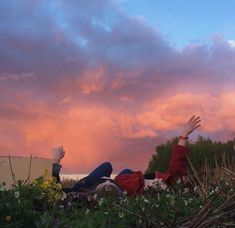 two people laying on the ground with their arms up in the air as the sun sets