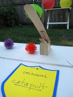 a paper plate and some crafting supplies on top of a white table with a yellow sign that says dragon catapult