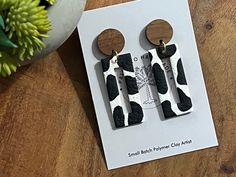 two pairs of earrings with black and white designs on them sitting on top of a wooden table