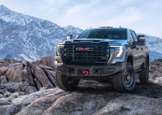 the front end of a gray truck parked on top of a rocky hill with mountains in the background