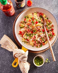 a white bowl filled with rice and vegetables next to a bottle of sauce on top of a table