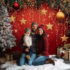 a man and woman sitting next to a christmas tree in front of a red backdrop