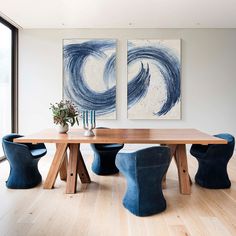 two paintings hang above a wooden table with blue chairs