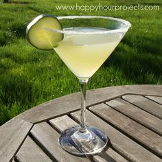 a margarita sitting on top of a wooden table with a cucumber in it