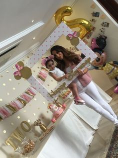 two women standing in front of a mirror with pink and gold decorations on the wall