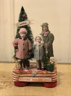 an old fashioned christmas card with two children and a small tree in the center, on a wooden table