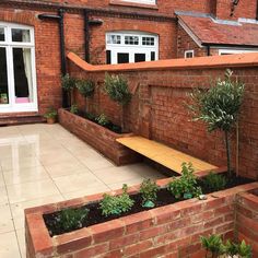 a brick building with a wooden bench next to it and plants in the foreground