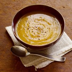 a brown bowl filled with soup next to two spoons on top of a wooden table