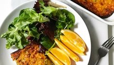 a white plate topped with food next to a bowl of salad and a pan of bread