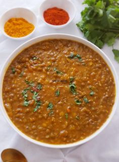 a white bowl filled with red lentula soup next to two bowls of spices and cilantro