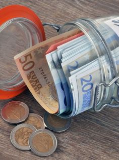 a jar full of money sitting on top of a wooden table next to some coins