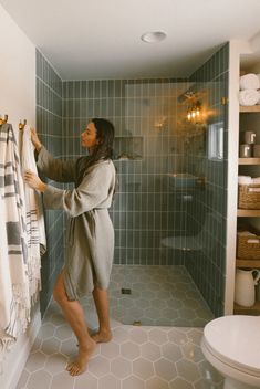 a woman is standing in the bathroom holding up her towel and looking into the shower