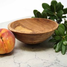 a wooden bowl sitting on top of a marble counter next to an apple and leafy plant