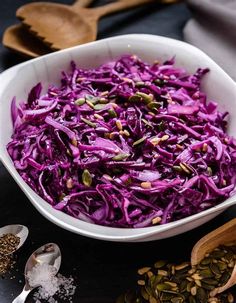 a white bowl filled with red cabbage next to spoons and seasoning flakes