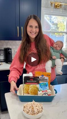 a woman holding a baby in her arms while standing next to a bowl of food