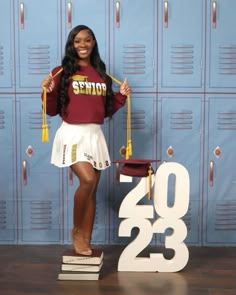 a woman standing in front of lockers holding a graduation cap and tassle