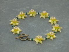 a bracelet with yellow flowers and green beads is shown on a gray surface in front of a grey background