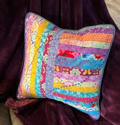 a colorful patchwork pillow sitting on top of a purple blanket