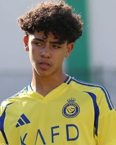 a young man with curly hair wearing a yellow soccer uniform and looking at the camera