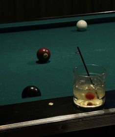 a pool table with some balls and a drink on it