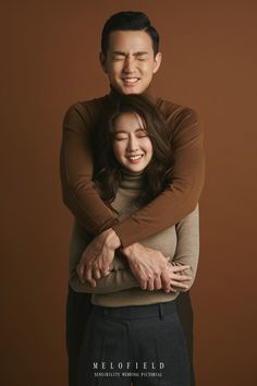 a man and woman hugging each other in front of a brown background