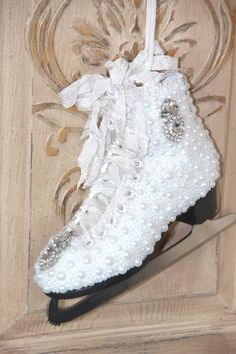 a pair of white snow boots hanging on a wooden door handle with beads and bows